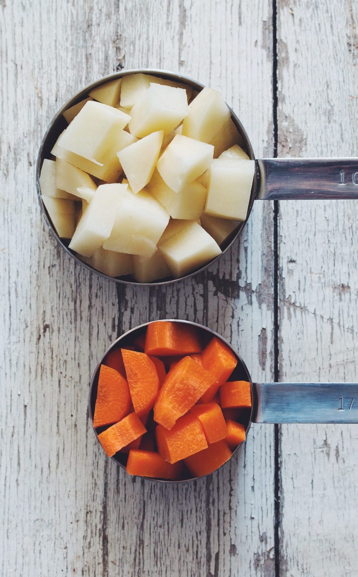 overhead of cubed potatoes and carrots in measuring cups