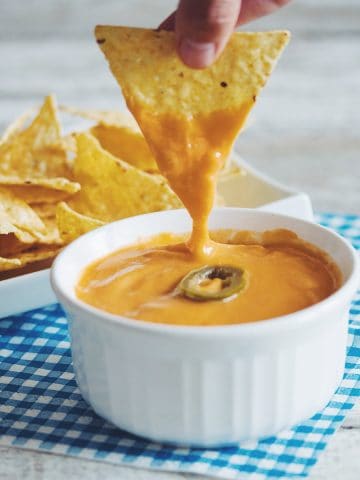 a tortilla chip dipped in vegan nacho cheese