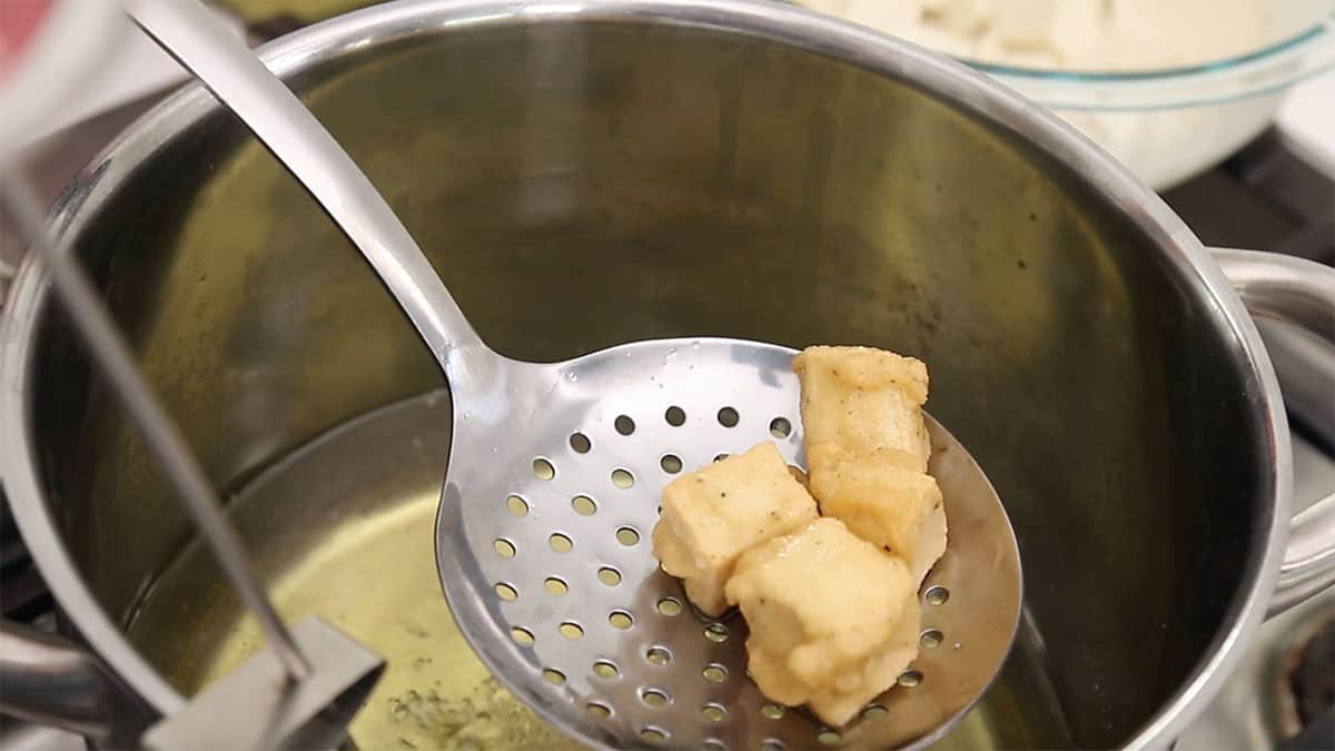 fried tofu cubes being lifted out of a pot of oil