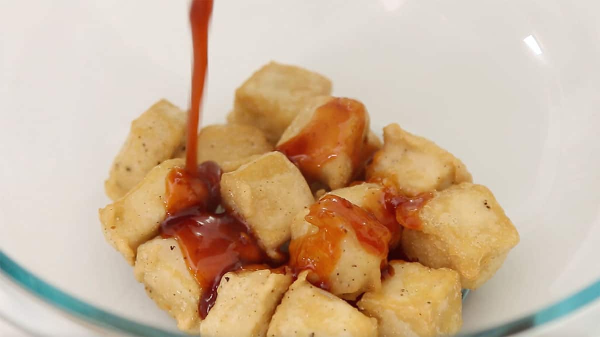 fried tofu with sweet and sour sauce being poured on top in a bowl