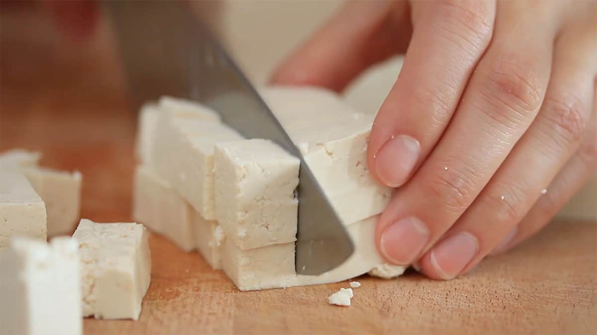 a knife cutting tofu into cubes