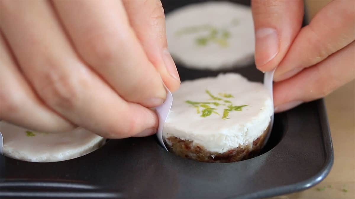 a mini vegan cheesecake bite being pulled out of the muffin pan with parchment tabs