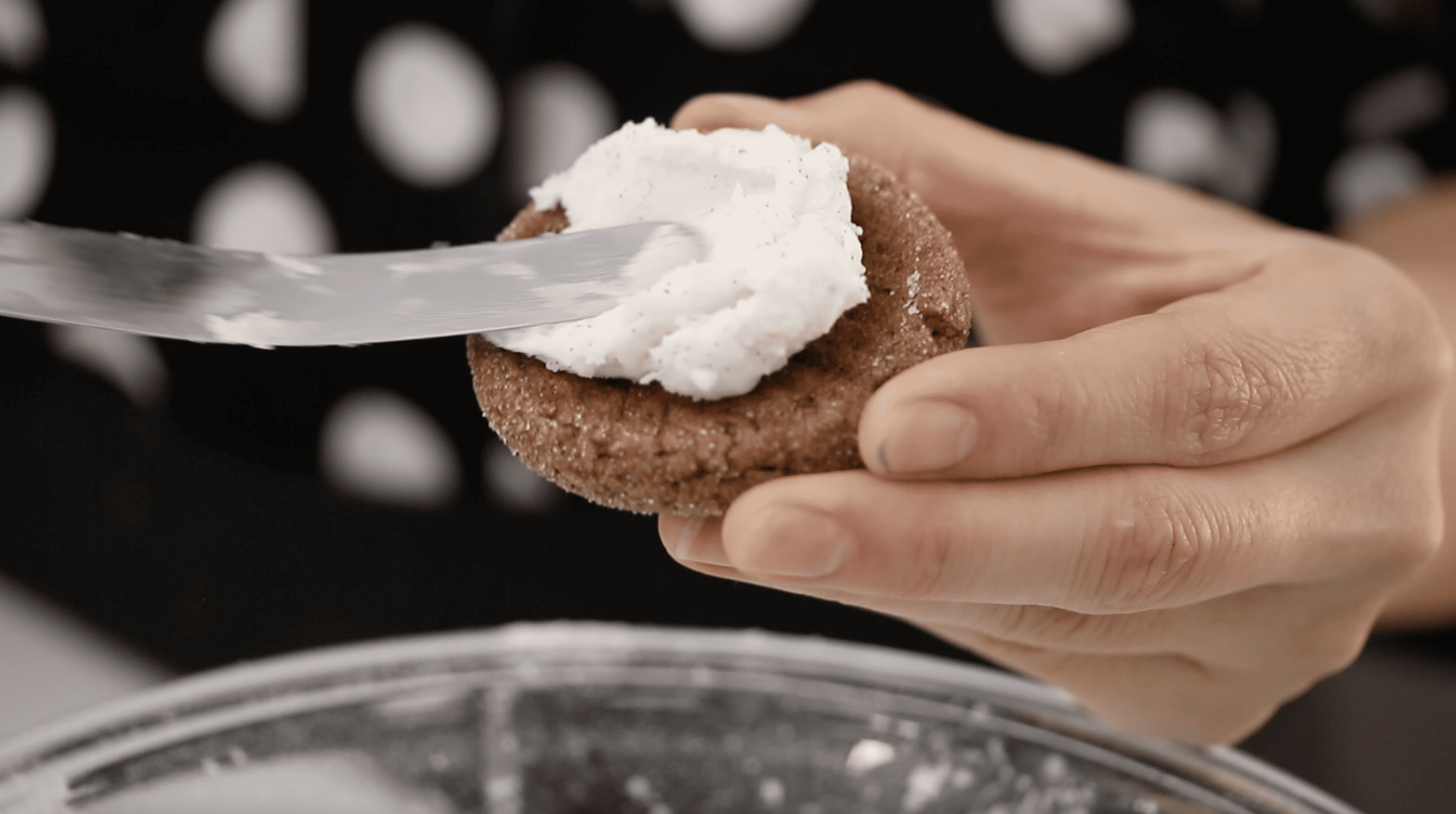a spatula spreading buttercream on the inside of a cookie