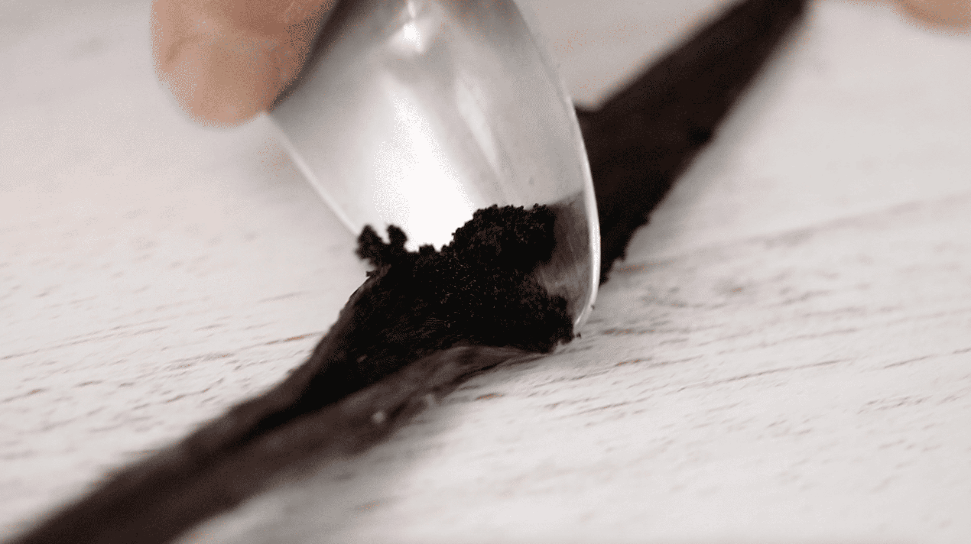 close up of a spoon scraping inside a vanilla bean