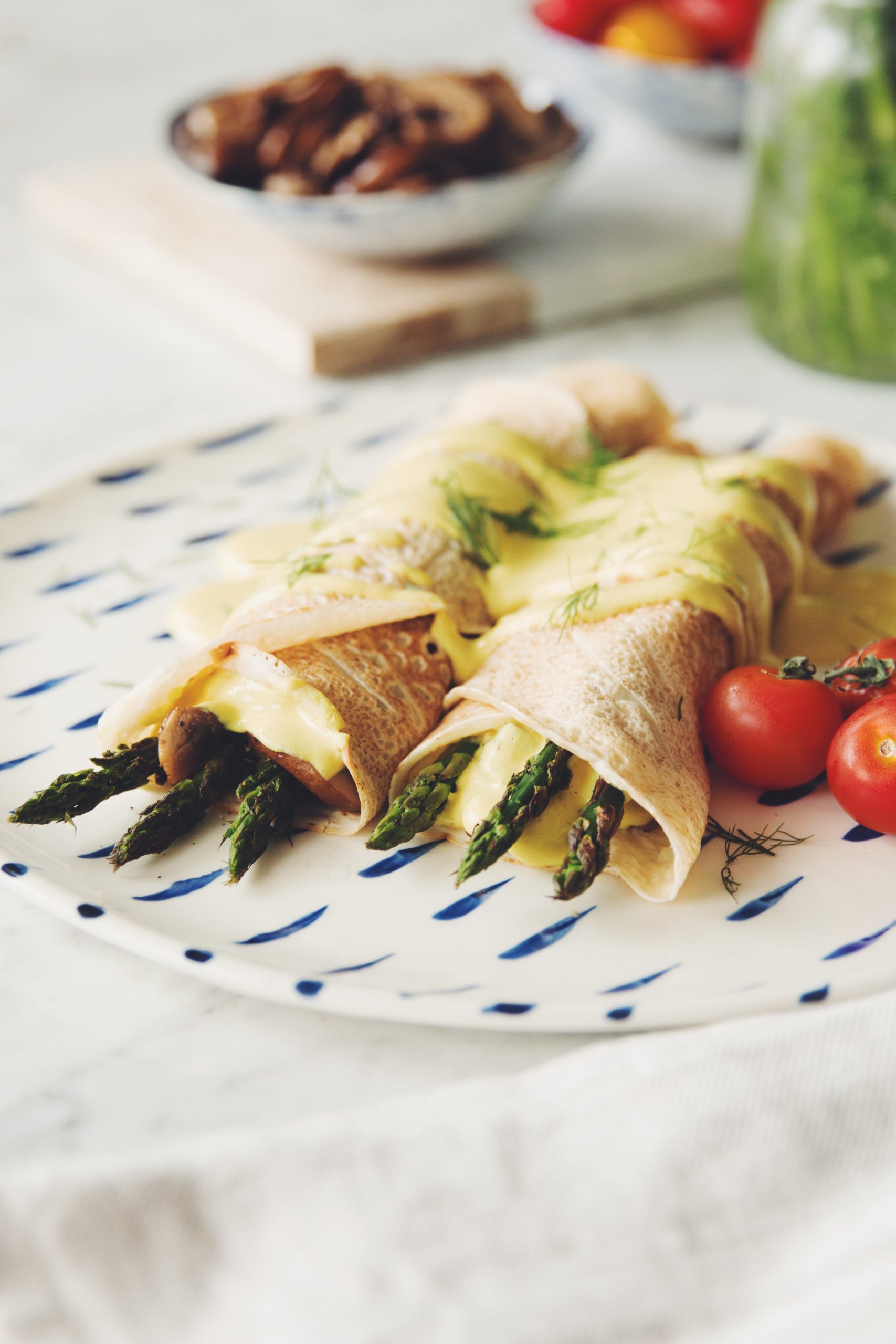 side angle of savory vegan crepes filled with asparagus and mushrooms and topped with hollandaise sauce