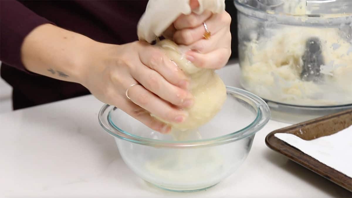 hands squeezing out water through a nut milk bag filled with shredded potato
