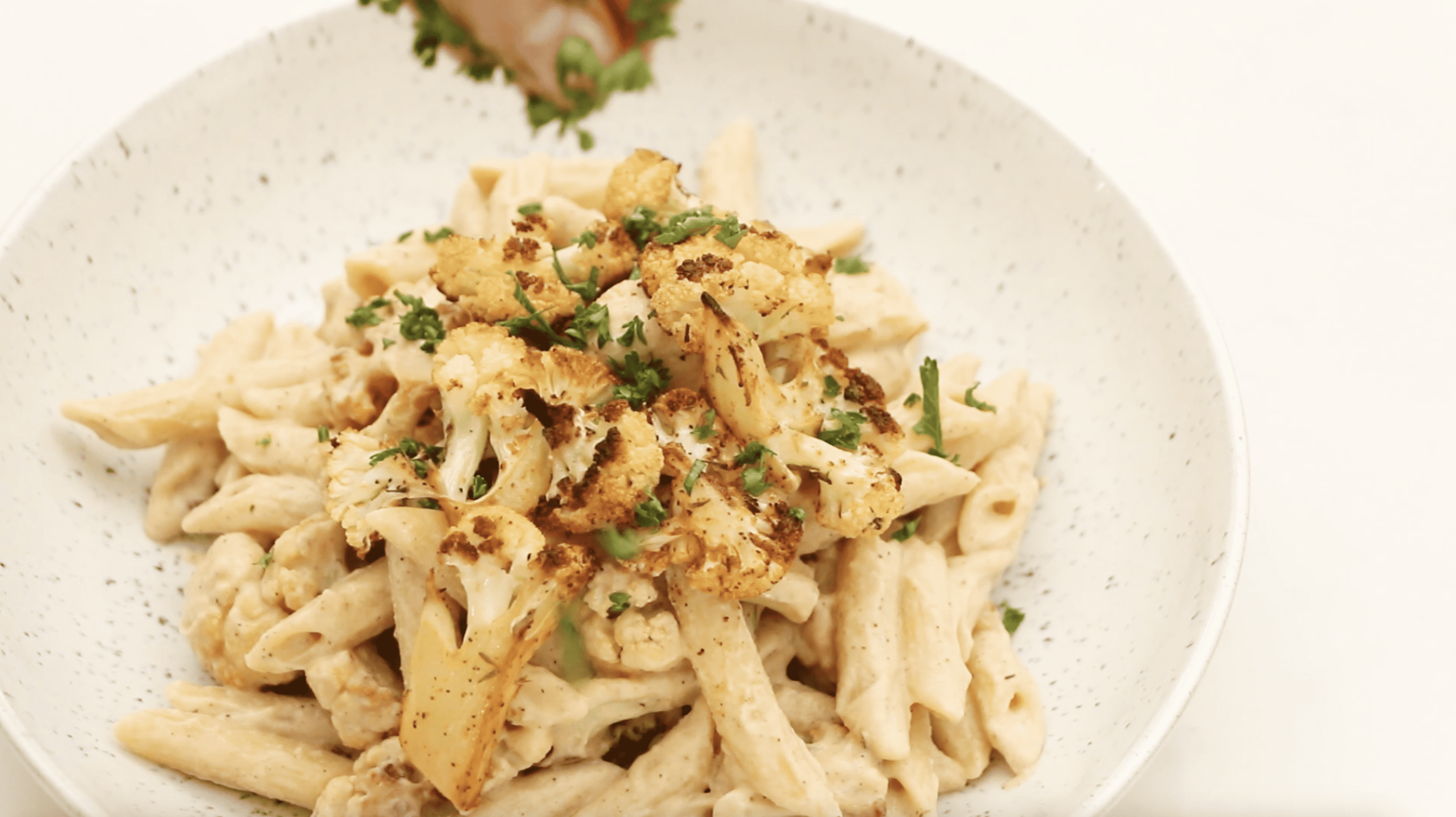 cauliflower alfredo pasta being garnished with parsley