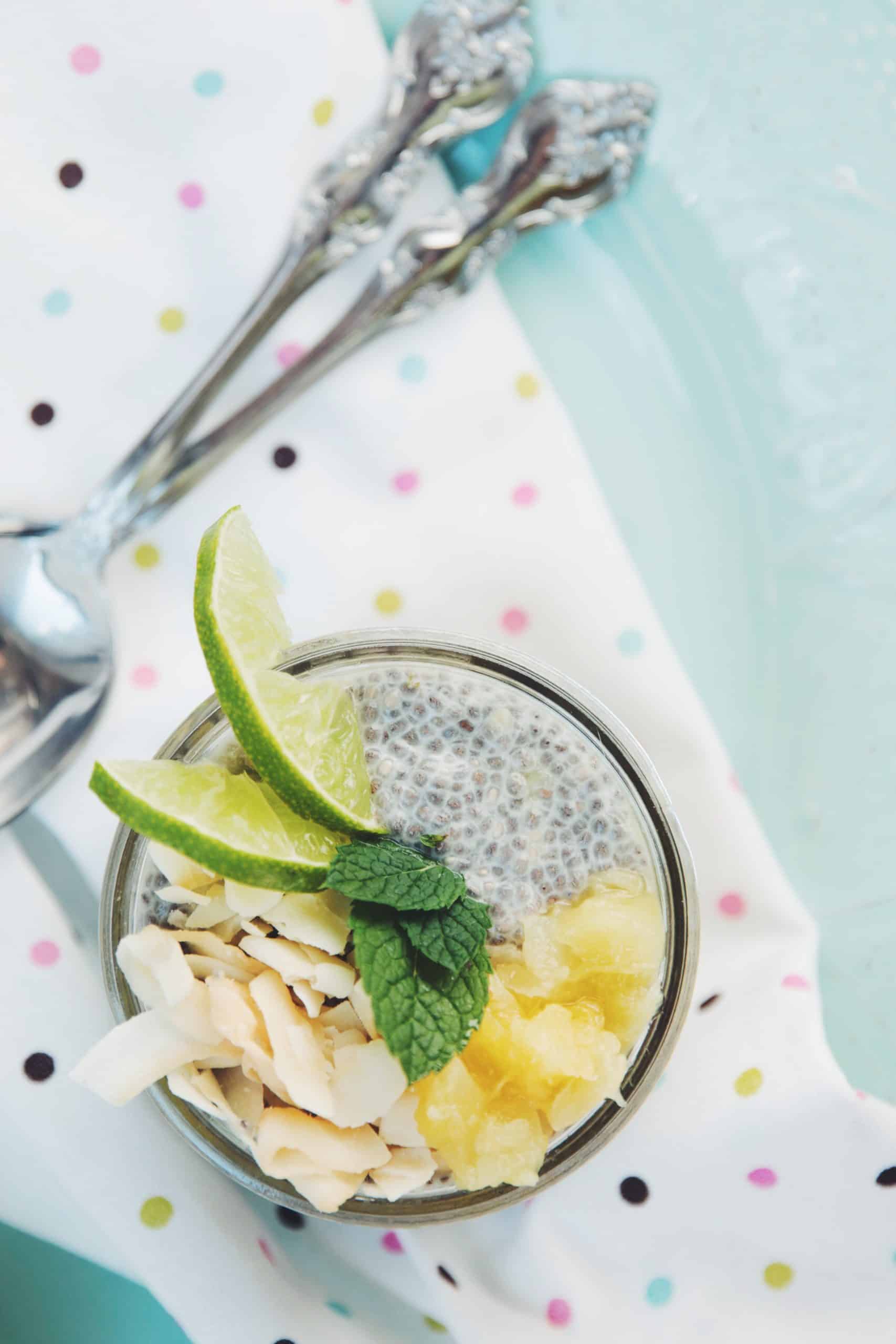 overhead view of a jar of chia pudding topped with pineapple, coconut flakes, and lime wedges