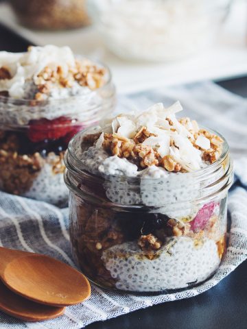 two jars of coconut milk and chia seed pudding parfaits with mixed berries and granola